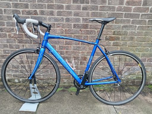 Blue road bike with drop handlebars, parked against a brick wall.